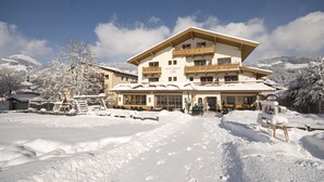 A multi-story building with a restaurant cafe on the ground floor, surrounded by snow-covered trees and mountains. - Loipenstub'n (Brixen im Thale)