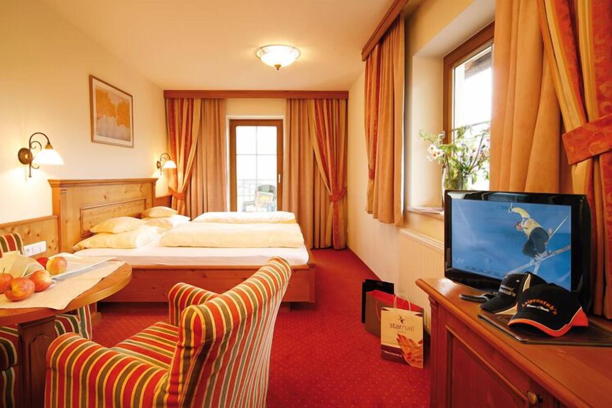 A hotel room with a bed, a desk with a computer, a television, and a window with curtains.