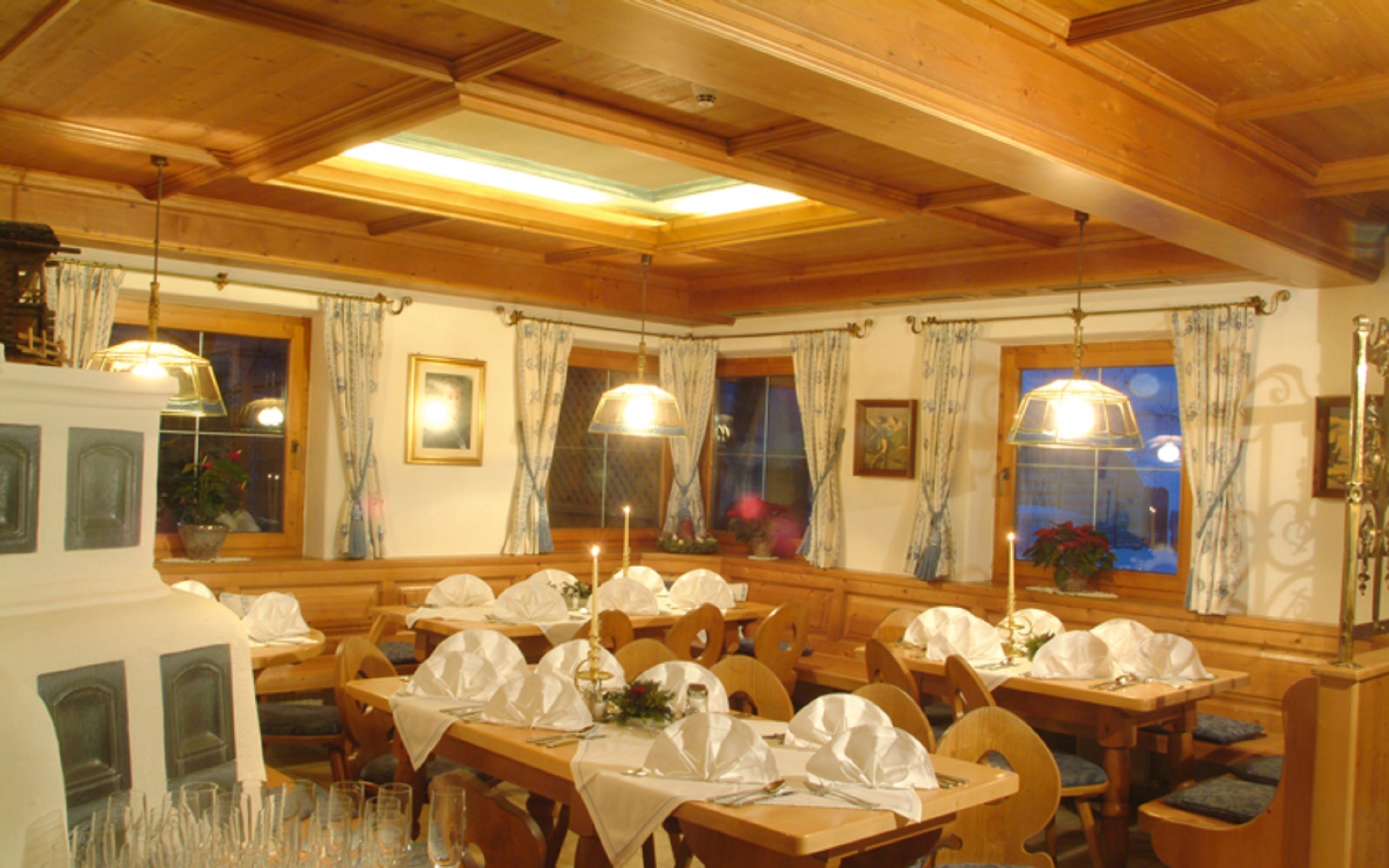 Un comedor con mesas y sillas de madera, cubiertas con manteles blancos y decorado con centros de mesa florales.