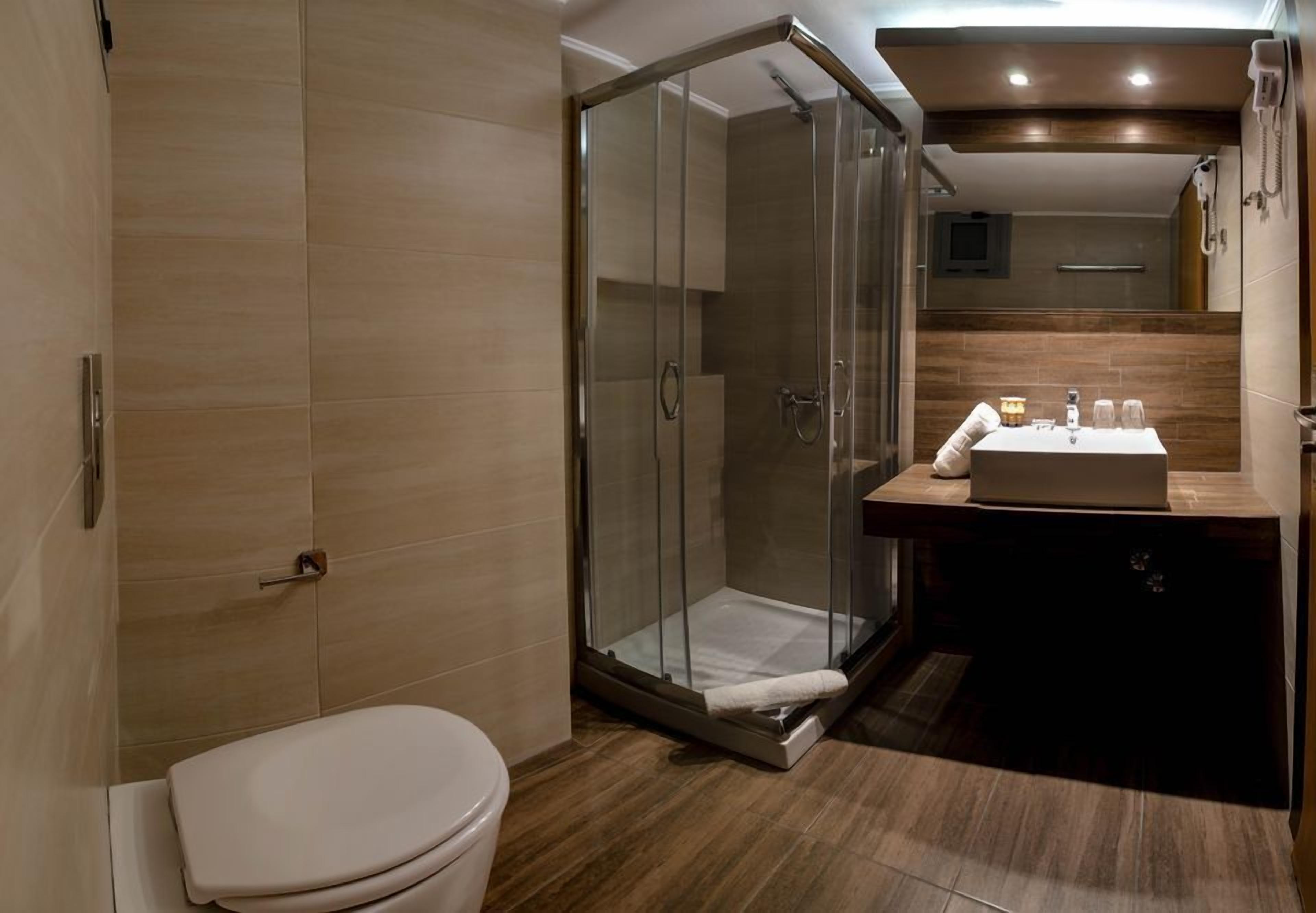 A modern bathroom with a glass-enclosed shower, a toilet, and a sink with a mirror above.