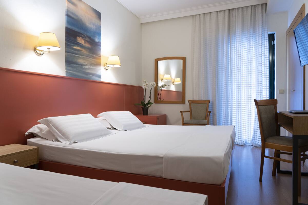 A hotel room with two beds, a desk, a chair, a mirror, and a painting on the wall.