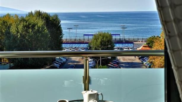 Een balkon met een tafeltje voor twee, met uitzicht op een parkeerplaats en de zee.