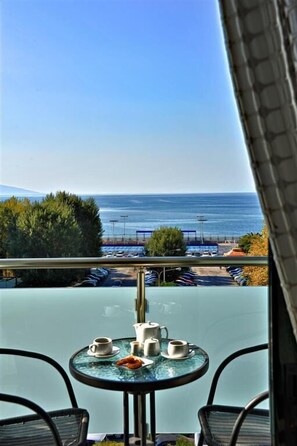 A balcony with a table set for two, overlooking a parking area and the sea. - Esperia Hotel (Kavala)