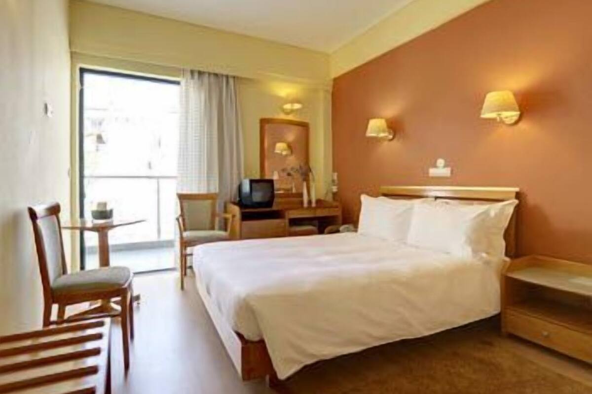 A hotel room with a bed, a desk, a chair, a television, and a window with curtains.