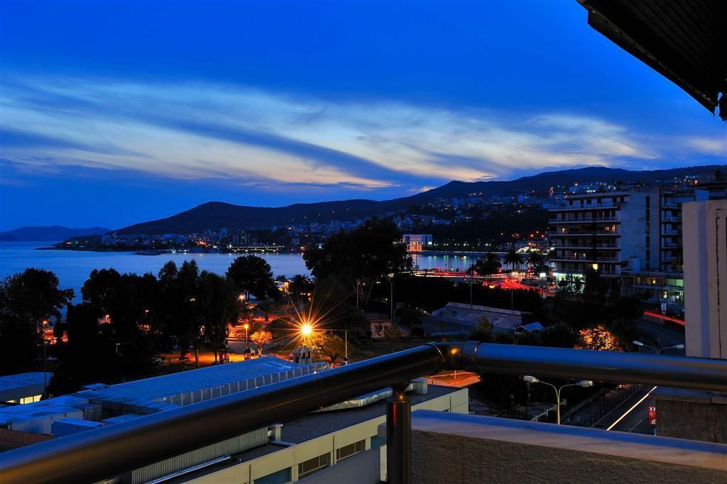 A coastal cityscape at dusk with a view of the sea and mountains in the background.