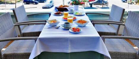 A dining area with a table set for breakfast, surrounded by wicker chairs, with a view of parked cars and buildings in the background.