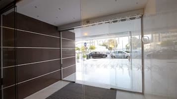 A modern hotel entrance with glass doors, a dark interior wall, and a view of the street outside.
