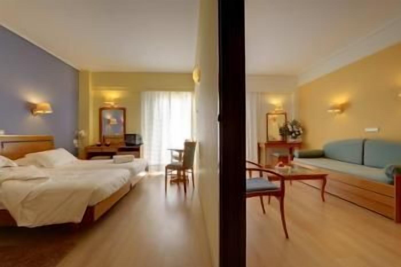 A hotel room with two beds, a desk, a chair, a sofa, and a small table.