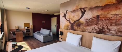 A hotel room with a large bed, a desk, a sofa, and a painting of a deer on the wall.