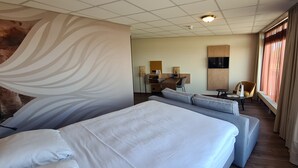 Een hotelkamer met een groot bed, een bank, een bureau met stoel, een aan de muur bevestigde televisie en een raam met gordijnen.