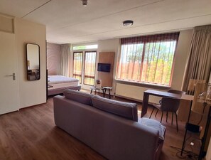 Une chambre d’hôtel avec un lit, un canapé, un bureau, une chaise, une télévision et une fenêtre avec des rideaux.