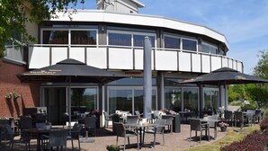 Een terras met tafels en stoelen, een bakstenen gebouw en grote parasols.