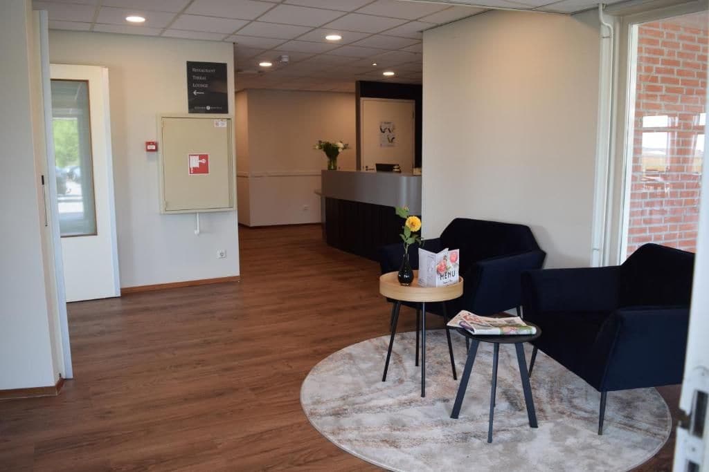 A reception area with a reception desk, a small table with a vase and a menu, and two chairs.