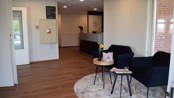A reception area with a reception desk, a small table with a vase and a menu, and two chairs.
