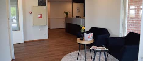 A reception area with a reception desk, a small table with a vase and a menu, and two chairs.