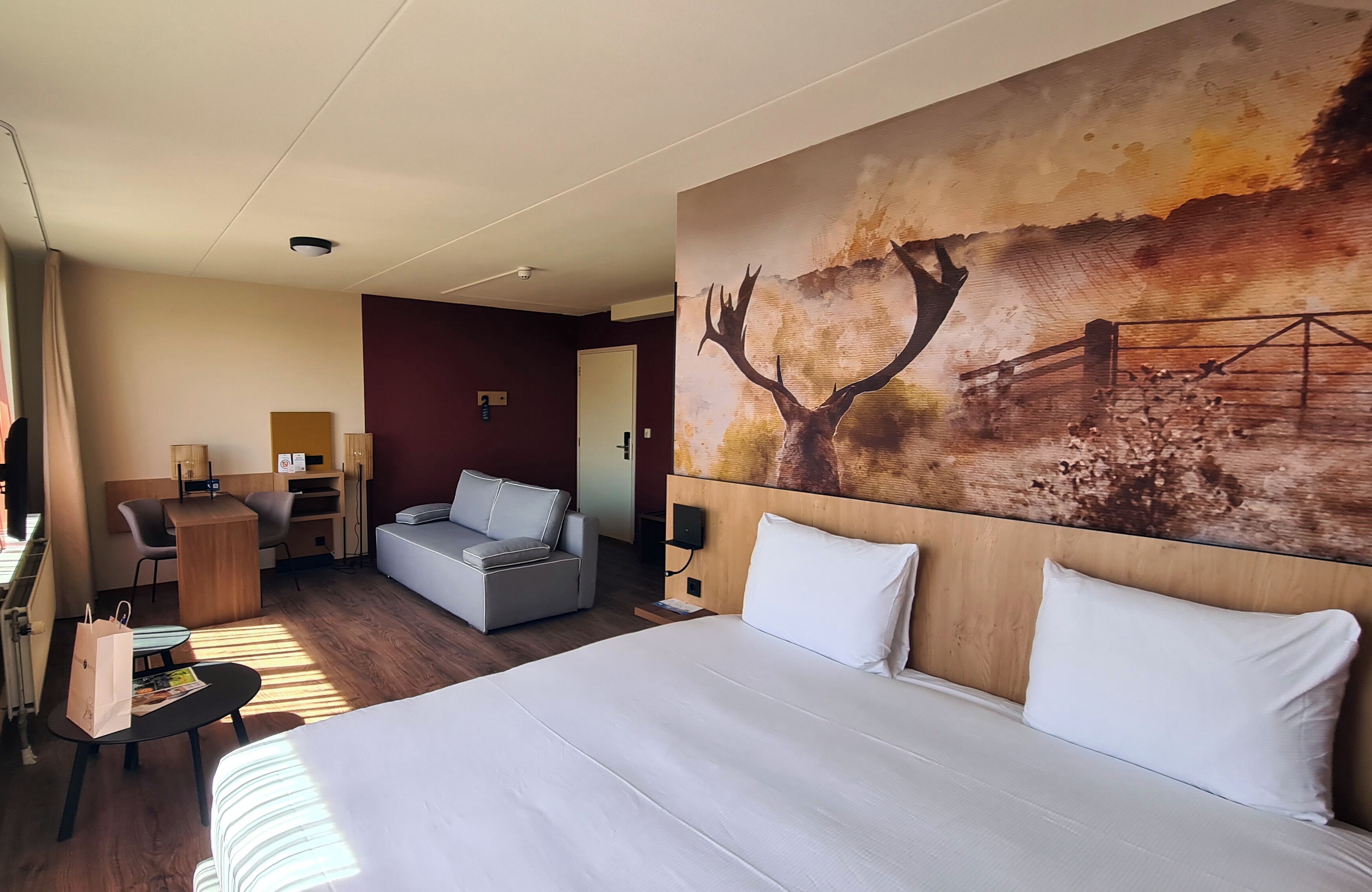 Une chambre d’hôtel avec un grand lit, un bureau, un canapé et un tableau représentant un cerf et un pont, accroché au mur.