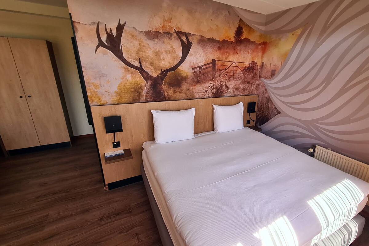 Een hotelkamer met een groot bed, een houten hoofdbord, twee nachtkastjes met lampen, een wanddecoratie en een houten garderobe.