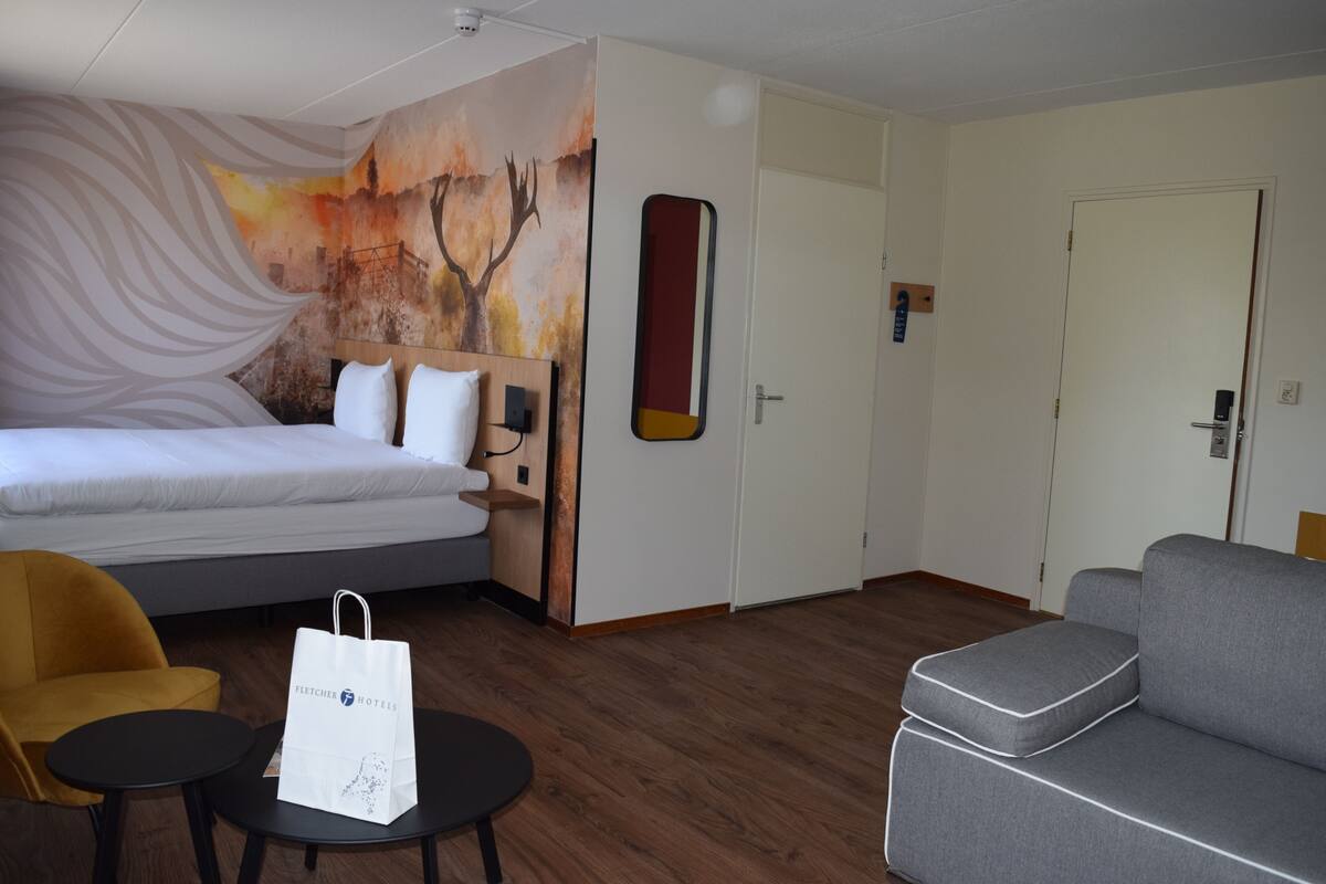 Een hotelkamer met een bed, een slaapbank, een tafeltje, een stoel, een schilderij en een spiegel.