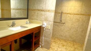 Baño con lavamanos, espejo y zona de ducha con barandilla.