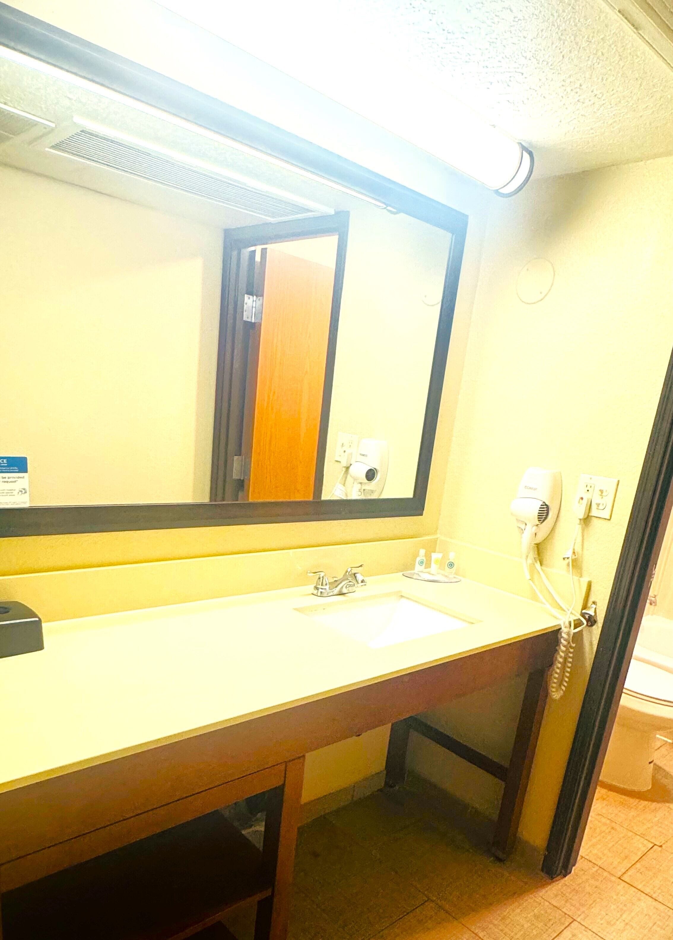 A hotel bathroom with a large mirror, a sink, a hairdryer, and a telephone.