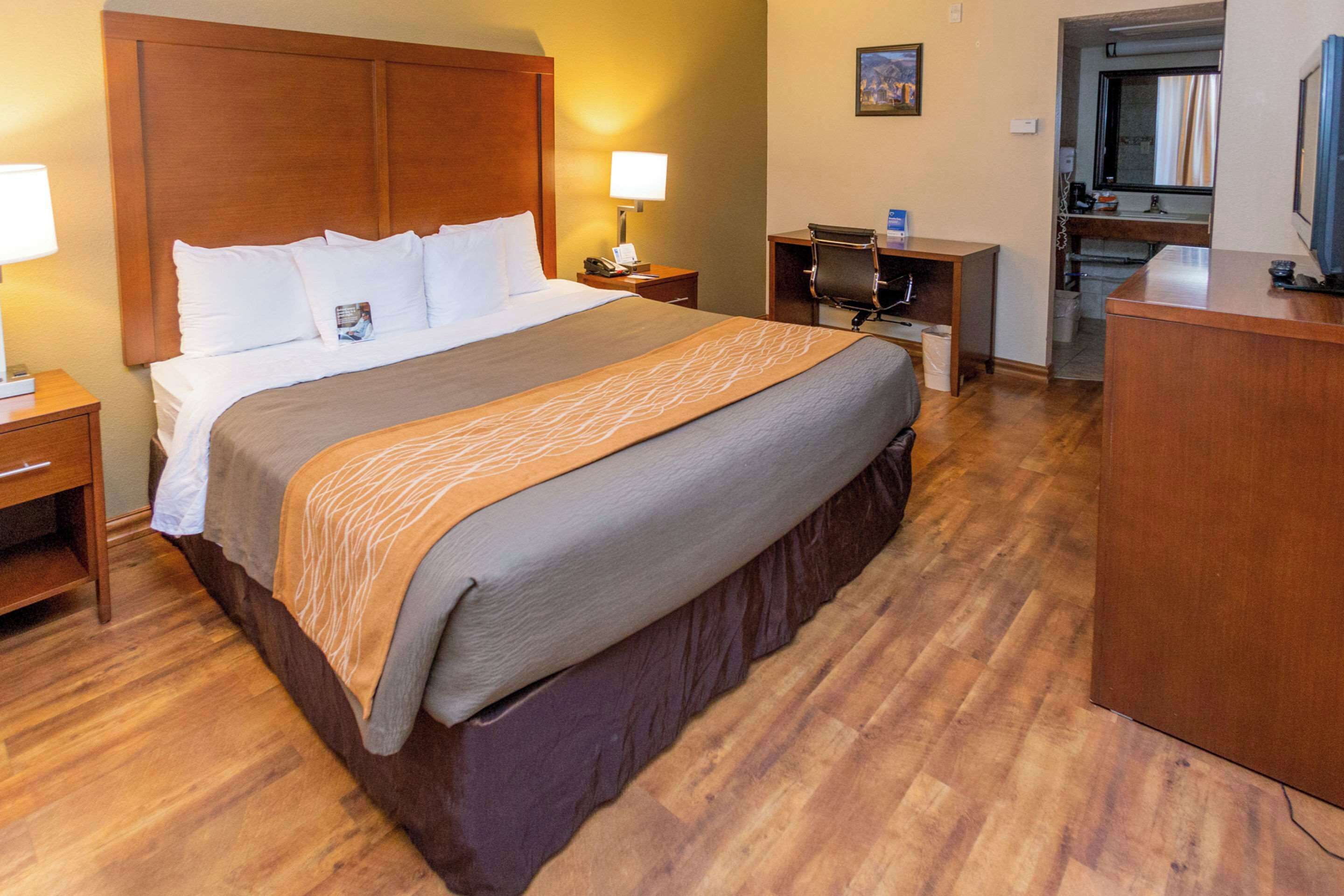 A hotel room with a large bed, wooden headboard, bedside tables with lamps, a desk, and a television.