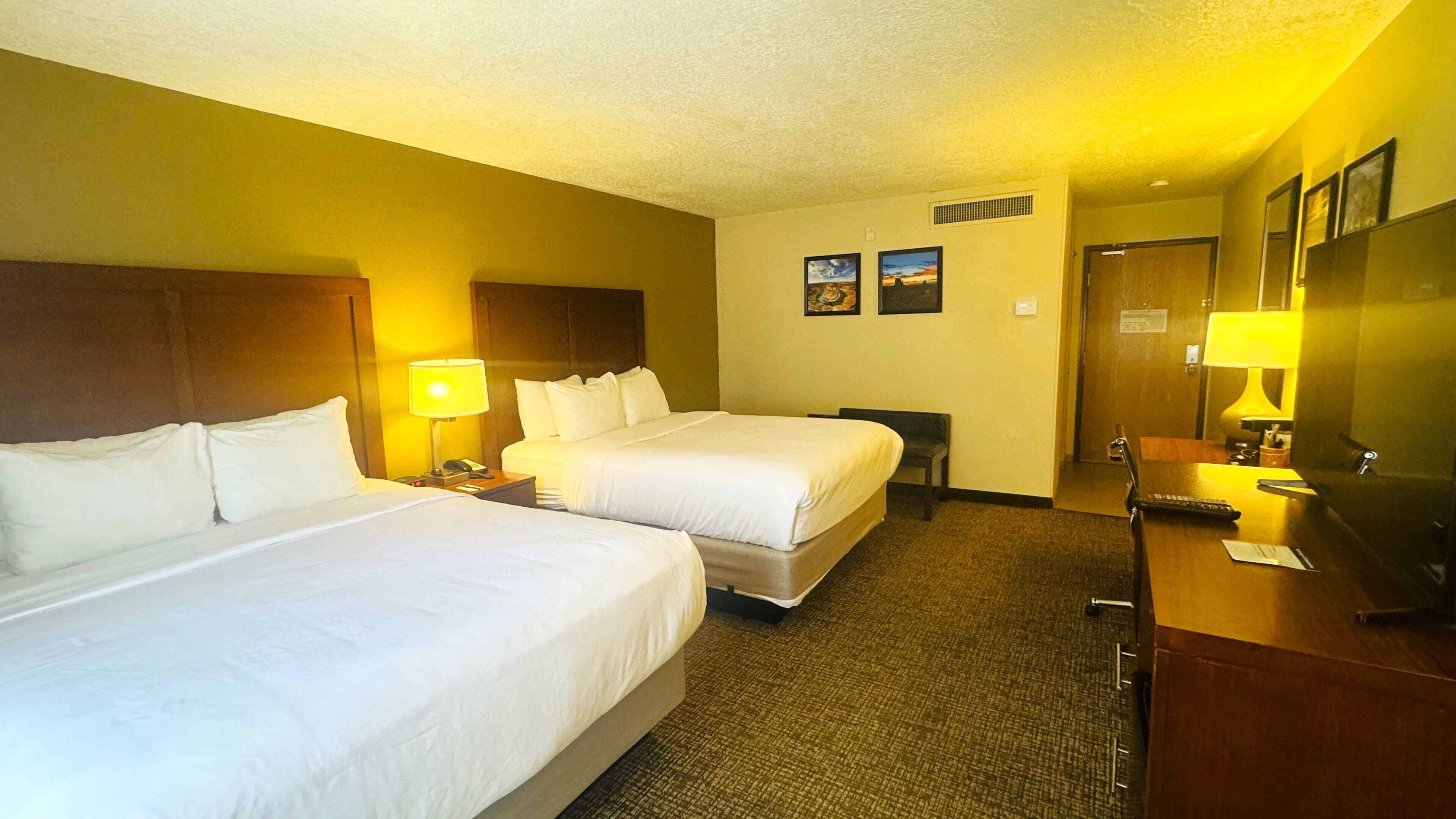 A hotel room with two beds, a desk with a lamp, a mirror, and a door.