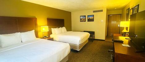 A hotel room with two beds, a desk with a lamp, a mirror, and a door.