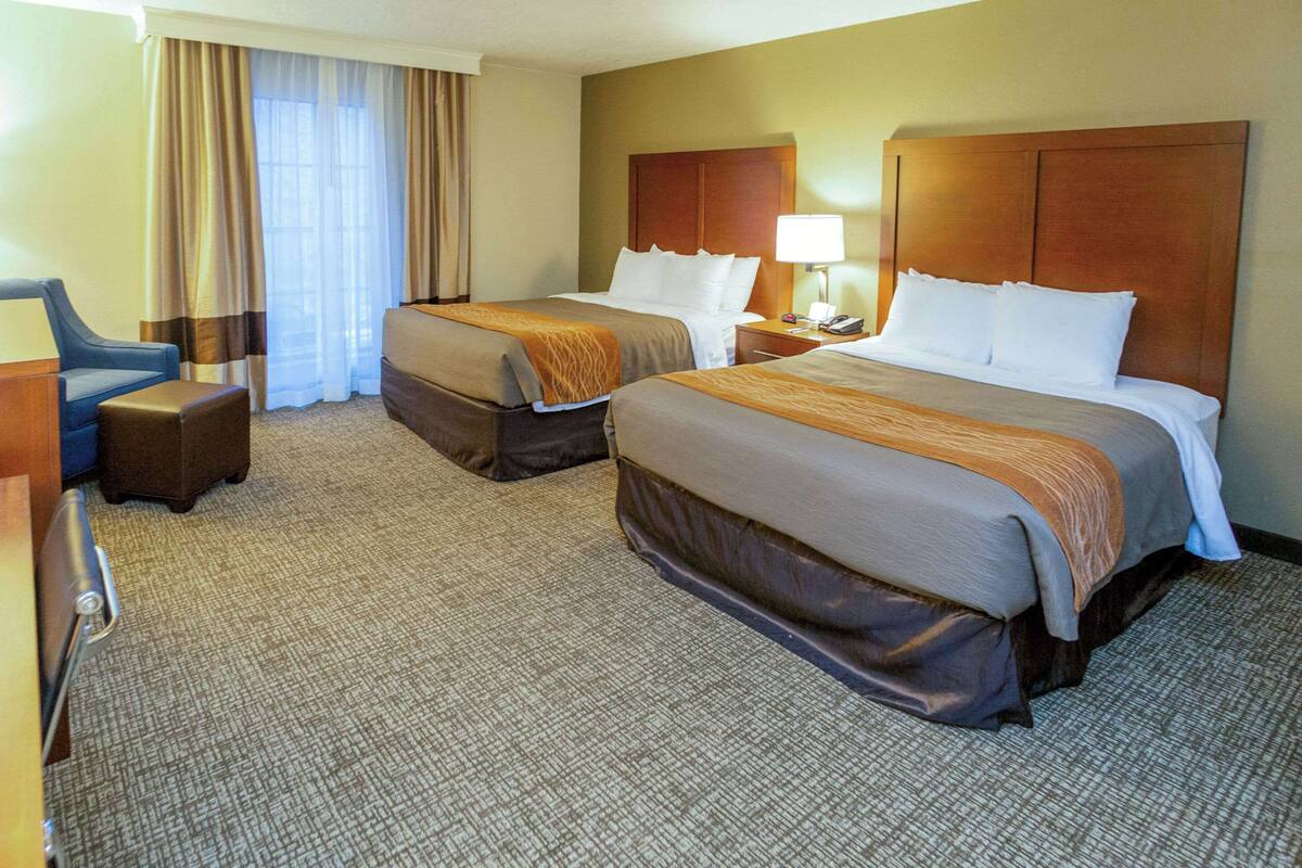 A hotel room with two beds, a desk, a chair, and a lamp.