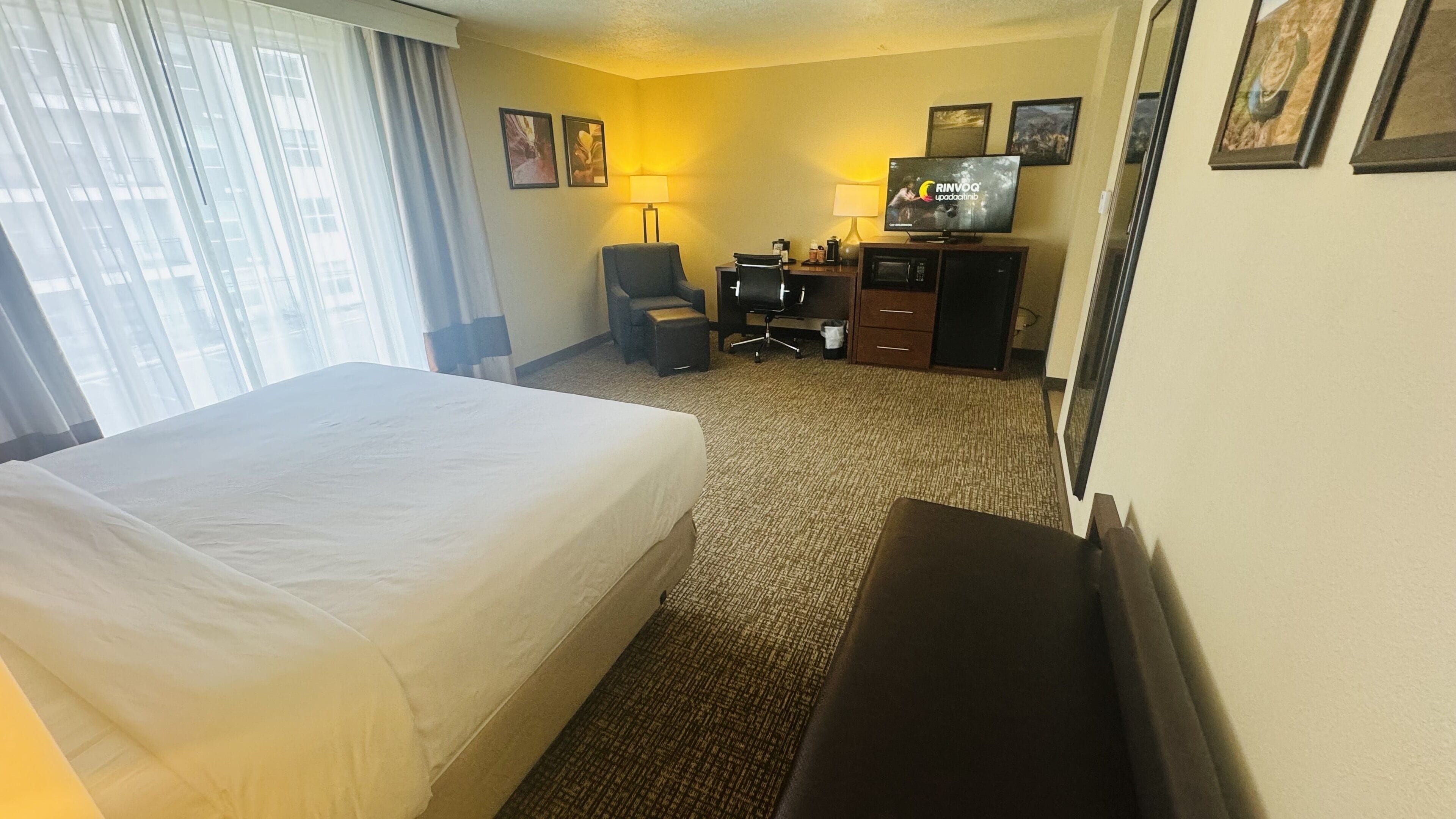 A hotel room with a large bed, a desk with a computer, a chair, and a TV.