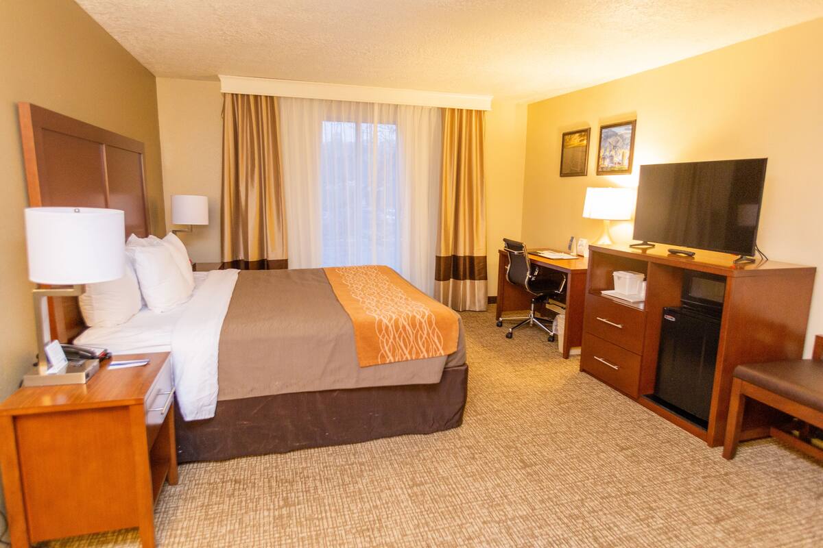 A hotel room with a bed, desk, TV, and a small kitchenette.