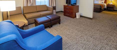 A hotel room with a sofa, a blue armchair, a TV, a desk, and a bed.