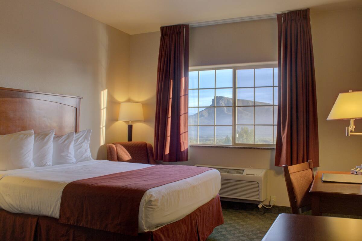 A hotel room with a large bed, two bedside lamps, a desk, and a view of a mountain through the window.