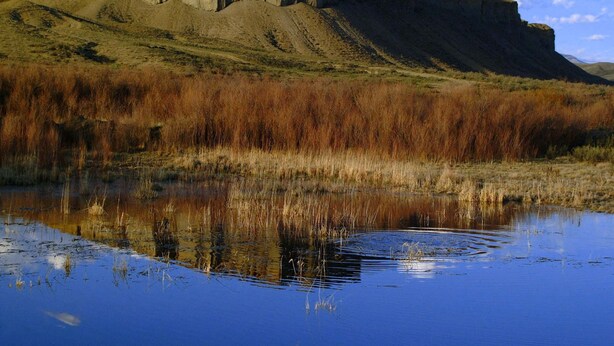 Paisaje natural con una gran colina y una masa de agua que refleja la colina.