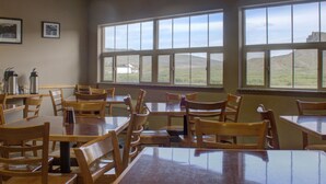 A dining area with wooden tables and chairs, large windows with a view of hills, and framed pictures on the wall. - Allington Inn & Suites (Kremmling)