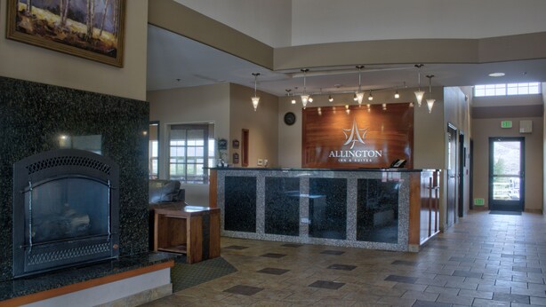 A reception area with a fireplace, a reception desk, and a sign for Allington Inn & Suites. - Allington Inn & Suites (Kremmling)