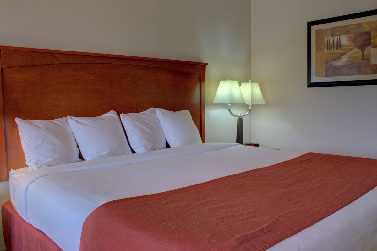 A hotel room with a large bed, a wooden headboard, white bedding, and a nightstand with two lamps.
