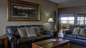 A living room with a dark leather sofa, a wooden coffee table, and a framed landscape painting on the wall. - Allington Inn & Suites (Kremmling)