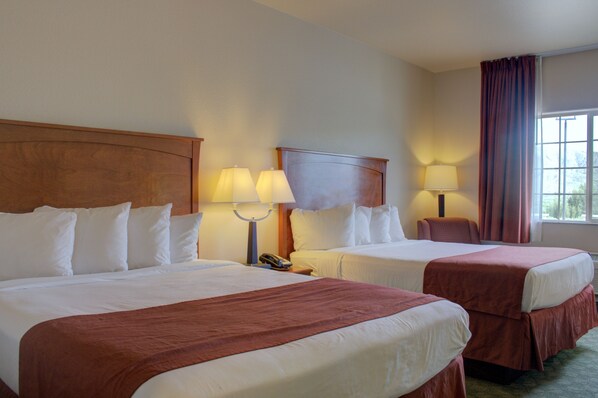 A hotel room with two beds, each with white linens and brown headboards. There are bedside lamps and a telephone on the nightstands.