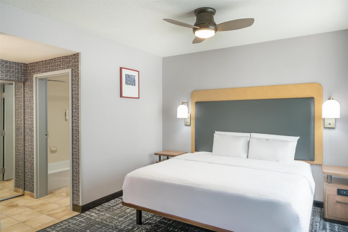 A hotel room with a bed, a ceiling fan, a nightstand, a bedside table, and a framed picture on the wall.