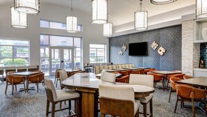 A spacious dining area with multiple tables and chairs, large windows, and a flat-screen TV mounted on the wall. - Homewood Suites by Hilton Pittsburgh Southpointe (Canonsburg)