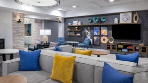 A modern living room with a grey sofa, blue and yellow cushions, a coffee table, and a TV mounted on the wall. - Homewood Suites by Hilton Pittsburgh Southpointe (Canonsburg)