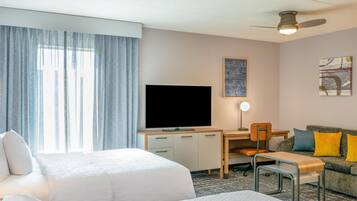 Hotelkamer met twee bedden, een bureau met televisie, een stoel, een bank met kussens en een plafondventilator.