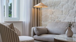 A room with a sofa, a striped chair, a floor lamp, and a vase on a table. - Heritage Hotel Kaštelet (Tucepi)