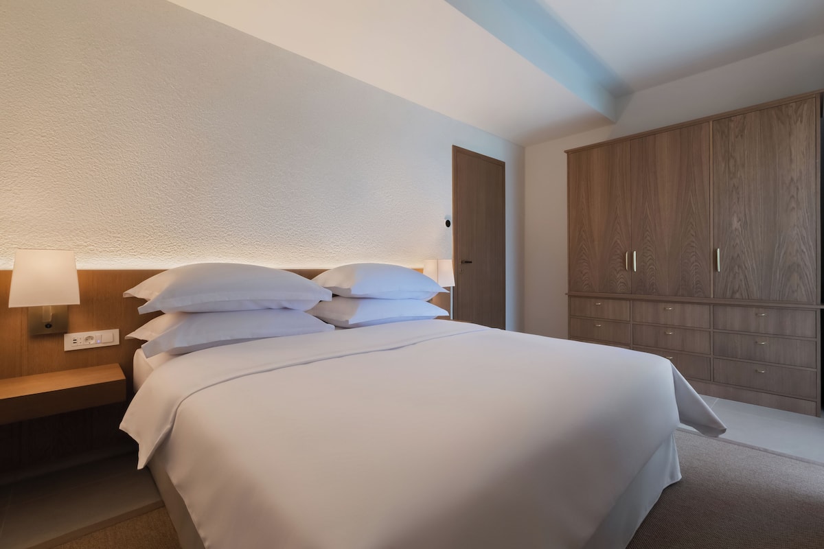 Et hotelværelse med en pænt redt seng, et sengebord med en lampe og en stor træskab.