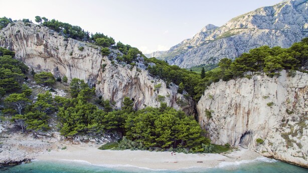 A coastal landscape with a sandy beach, rocky cliffs, and dense green vegetation. - Heritage Hotel Kaštelet (Tucepi)