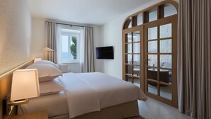 A hotel room with a bed, a TV, a window with curtains, and a view of the outdoors. - Heritage Hotel Kaštelet (Tucepi)