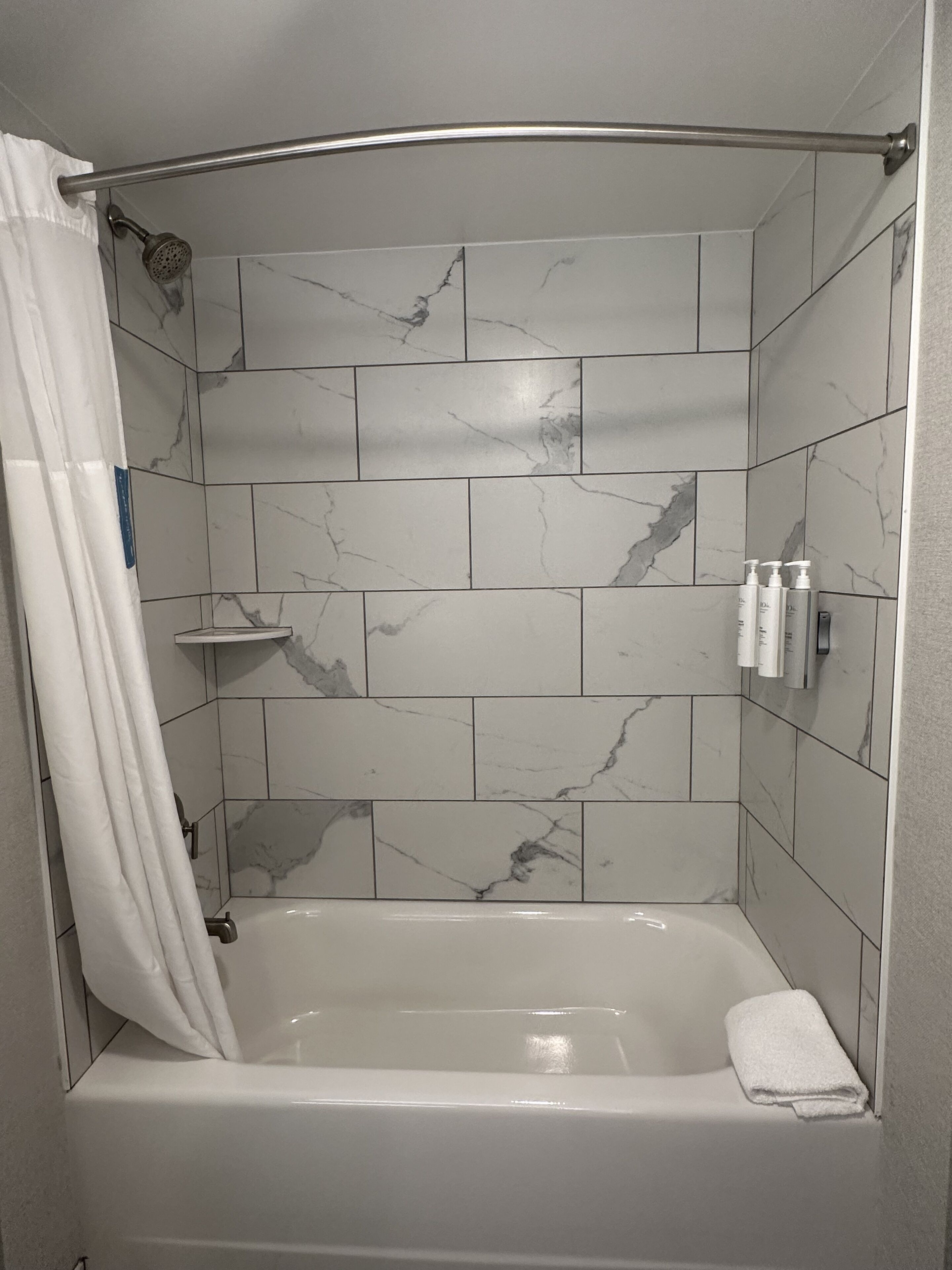 A modern bathroom with a freestanding bathtub, marble tiles, a shower curtain, and toiletries on a shelf.