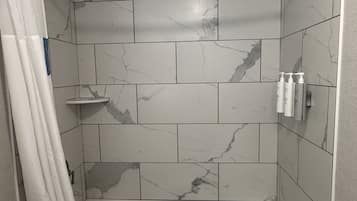 A modern bathroom with a freestanding bathtub, marble tiles, a shower curtain, and toiletries on a shelf.