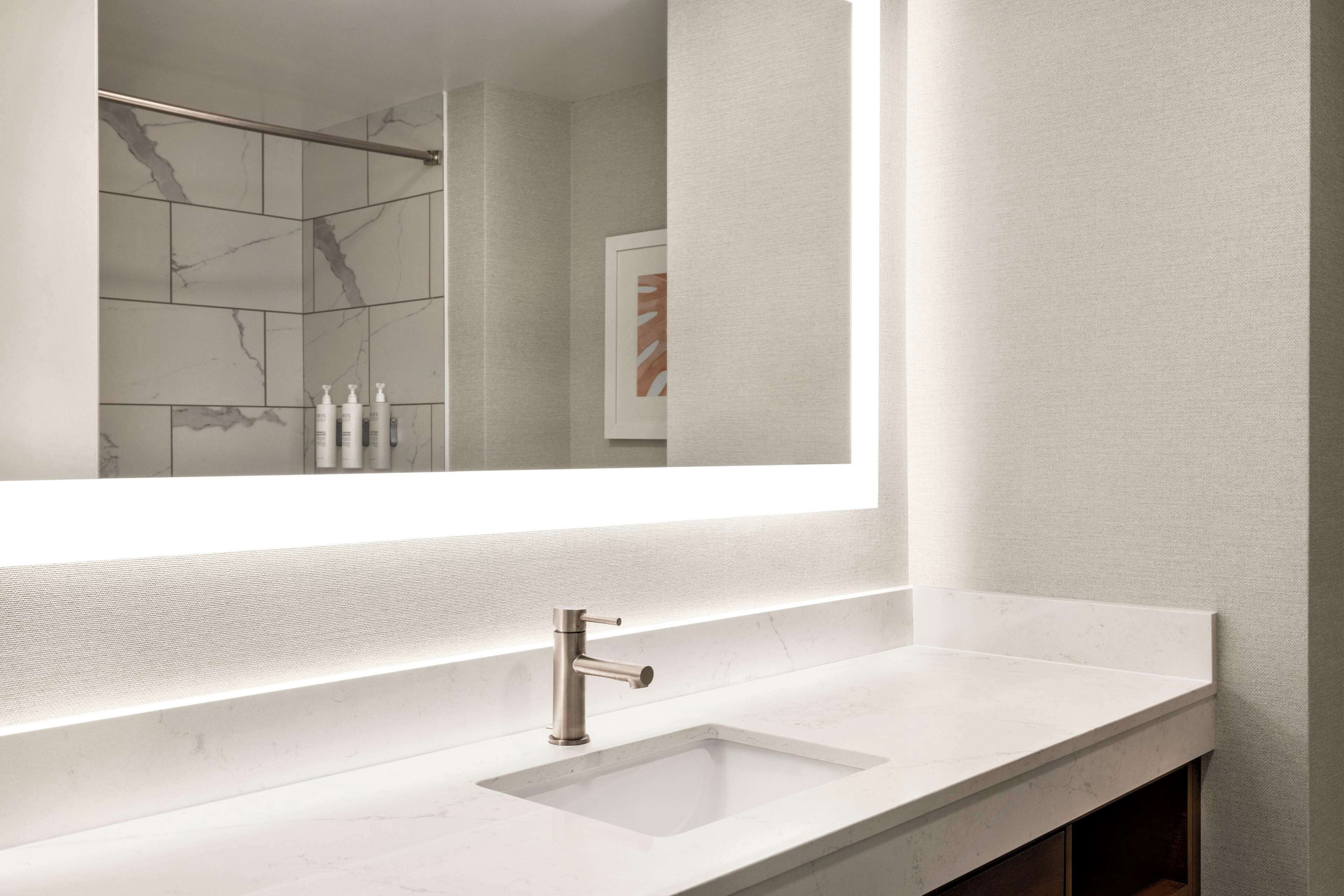 A modern bathroom with a large mirror, a white sink, and a shower area.