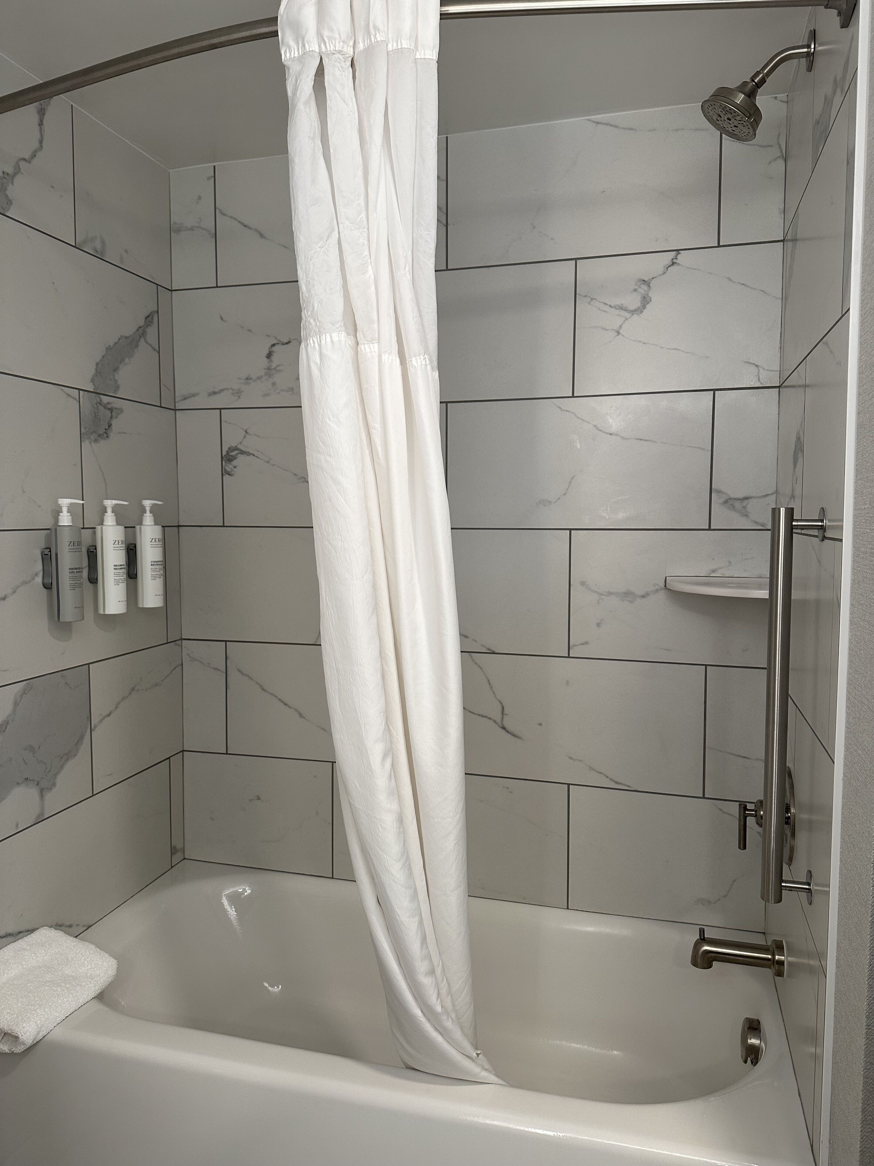 Un espace douche moderne avec un rideau blanc, des carreaux de marbre et une douchette à main.